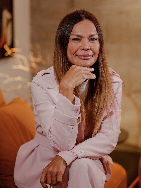 Dra. Cintia Borin sentada em um sofá, sorrindo, com a mão apoiada no queixo