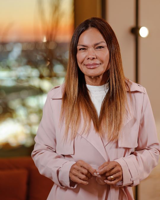 Dra. Cintia Borin em pé, sorrindo, com a vista da cidade ao entardecer ao fundo