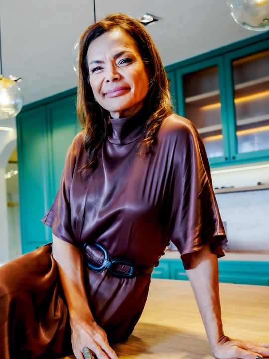 Dra. Cintia Borin sentada na bancada de uma cozinha, sorrindo para a câmera